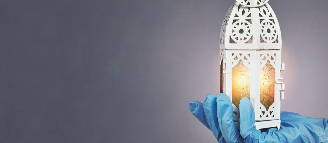 Ramadan 2020 in quarantine Hand in protective medical gloves holding traditional Arabic lantern with middle-eastern carving. Celebrating Holly month Ramadan 2020 in quarantine. A doctor celebrates Ramadan in hospital